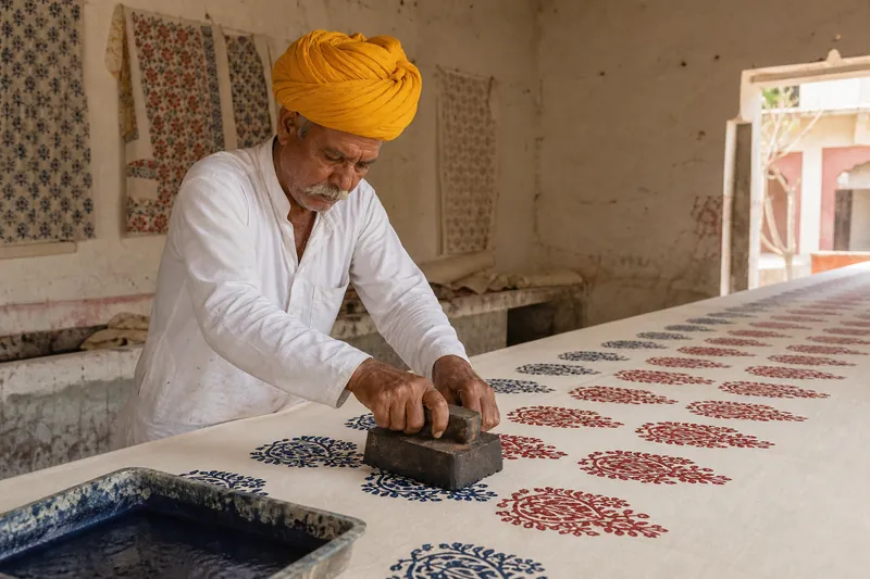 Artisan pressing a carved wooden block onto cotton in a Jaipur printing workshop